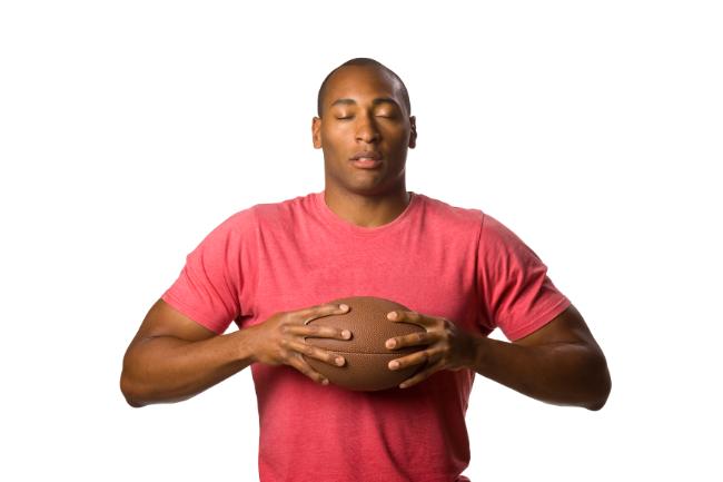 Football player holding a football with his eyes closed in contemplation. 